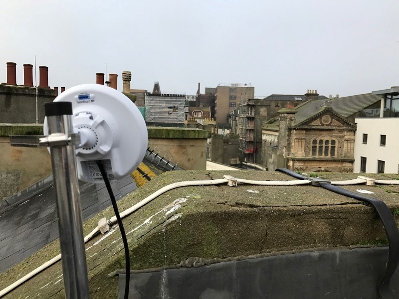Telecommunication disc in foreground aims at grey building on horizon 