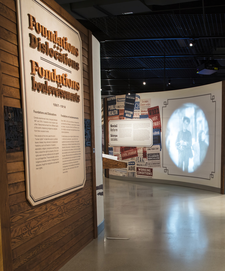 Wall containing raised text, cut of wood on the left-hand side, and a projection of a young boy on the right.