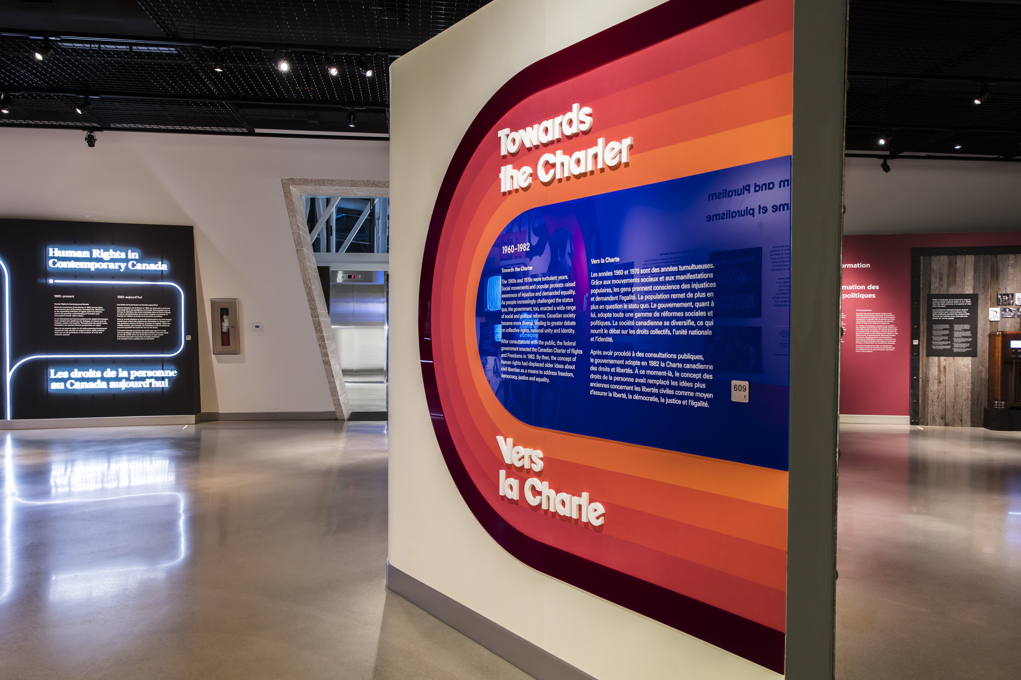 Evening interior image of walls containing text, with coloured plastic bars in a "U" shape pattern.