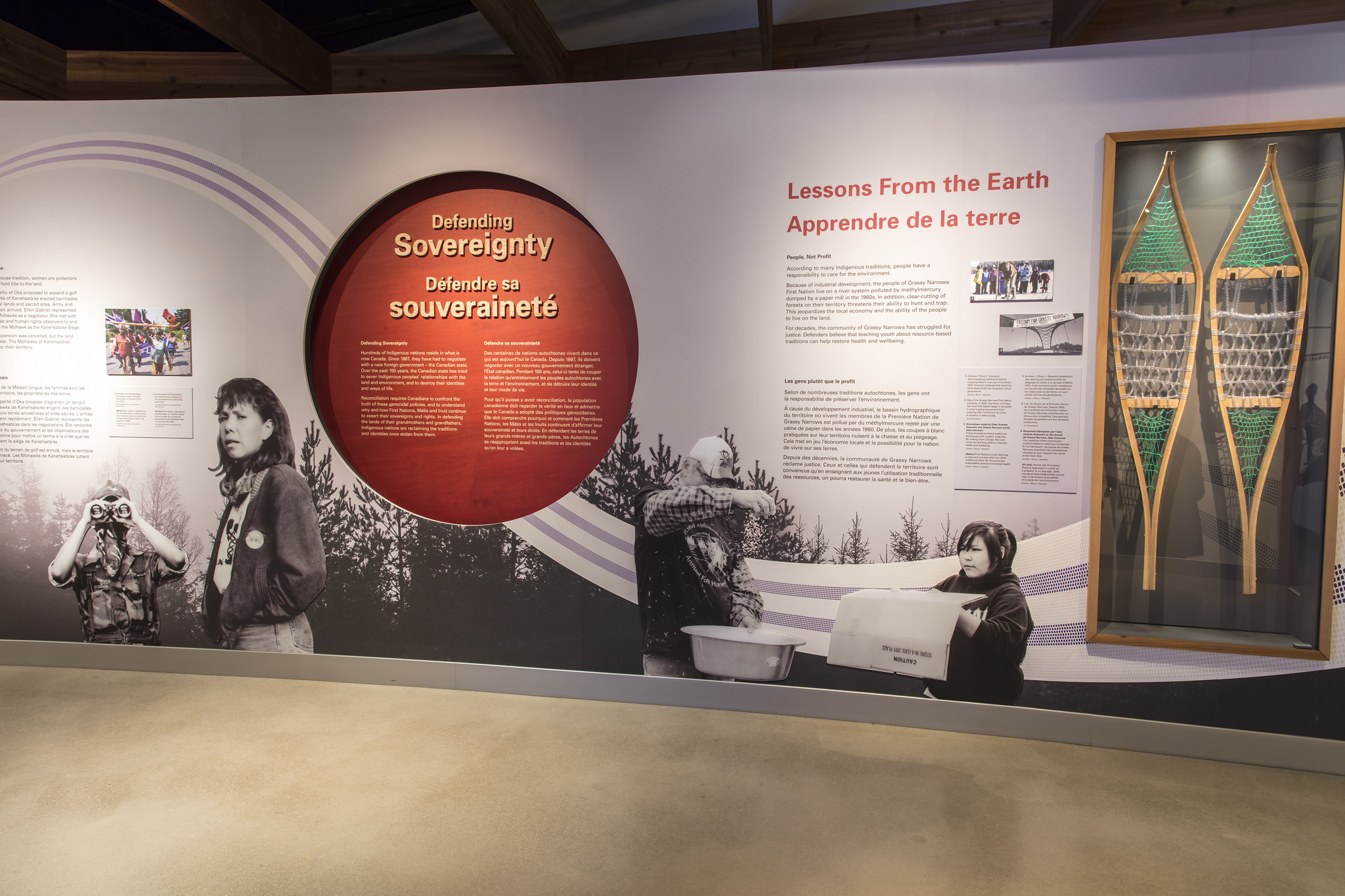 A wall with a depressed red circle in the center containing exhibition text on the left. To the right, a pair of show shoes in a glass case.