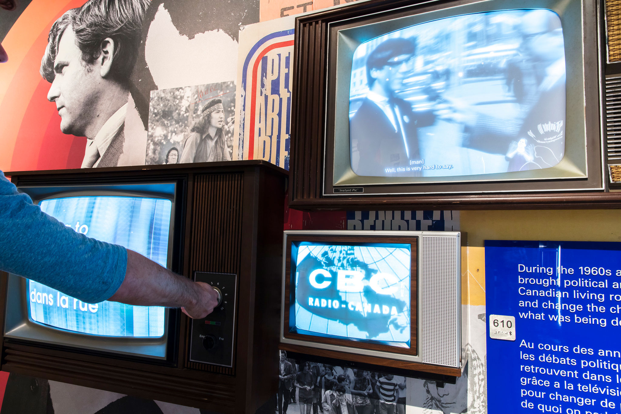 Three television screens take up most of the image. A hand reaches in from the left, turning the dials on the left-most television.